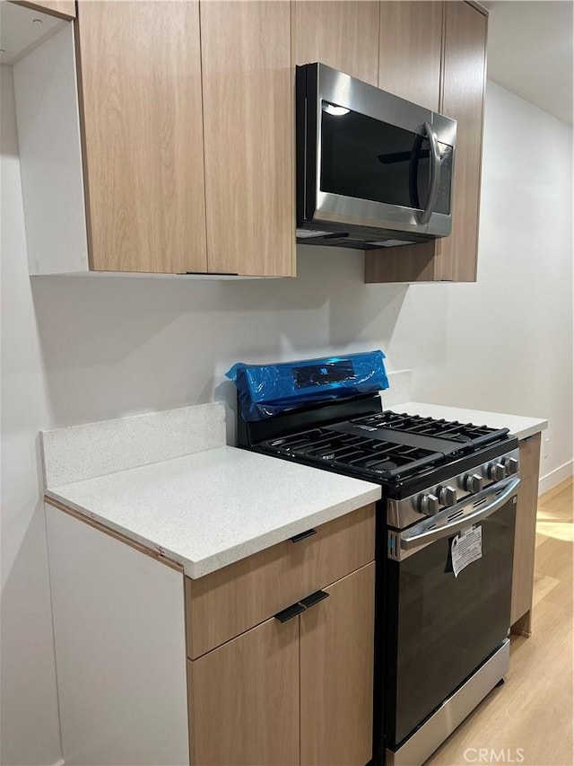 kitchen featuring light countertops, appliances with stainless steel finishes, light brown cabinets, modern cabinets, and light wood-type flooring