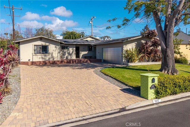 single story home featuring decorative driveway, an attached garage, a front yard, and stucco siding