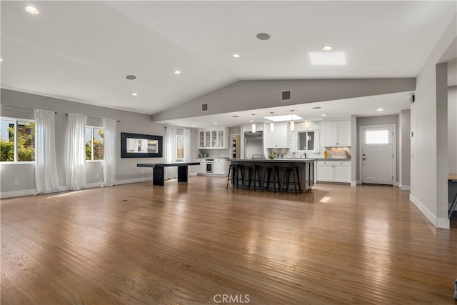 unfurnished living room with vaulted ceiling, visible vents, baseboards, and wood finished floors