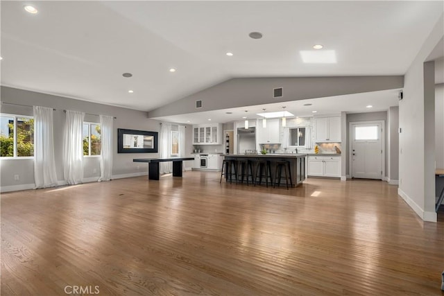unfurnished living room featuring vaulted ceiling, a wealth of natural light, wood finished floors, and visible vents