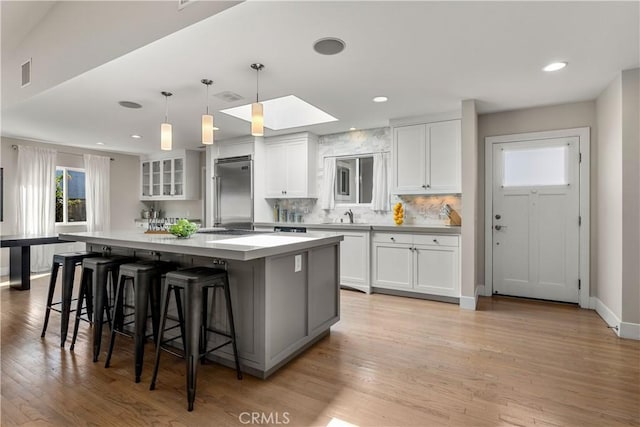 kitchen with a breakfast bar area, visible vents, a large island, white cabinetry, and stainless steel built in refrigerator