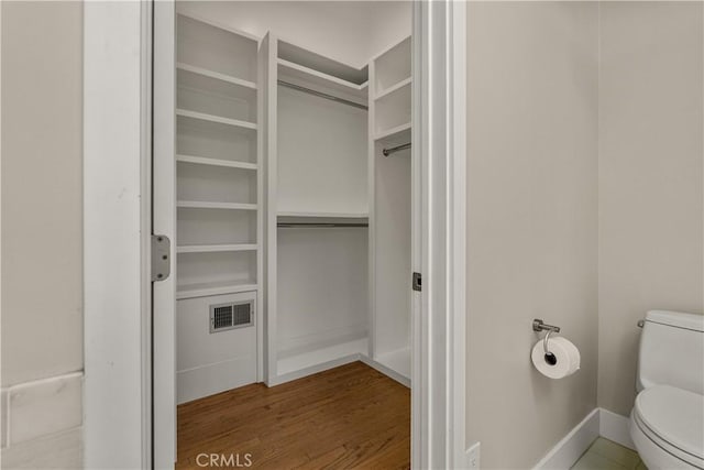 bathroom featuring visible vents, wood finished floors, baseboards, toilet, and a spacious closet