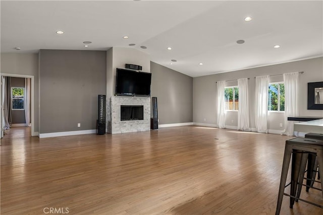 living area featuring baseboards, lofted ceiling, a premium fireplace, recessed lighting, and wood finished floors