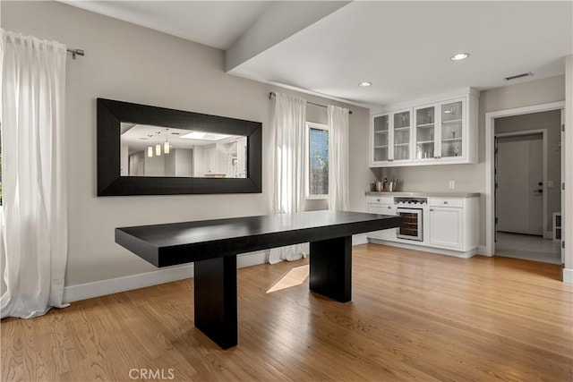 unfurnished dining area featuring light wood-style floors, visible vents, a bar, and beverage cooler