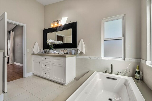 full bathroom featuring double vanity, tile patterned floors, a soaking tub, and a sink
