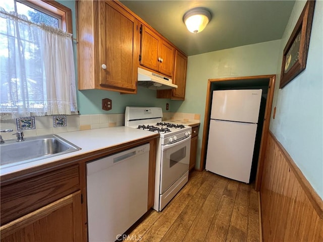 kitchen with brown cabinets, light wood-style flooring, a sink, white appliances, and under cabinet range hood