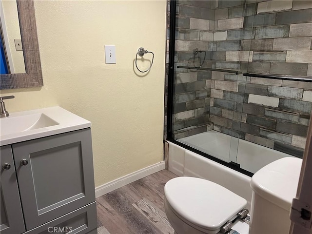 bathroom featuring toilet, wood finished floors, vanity, baseboards, and combined bath / shower with glass door