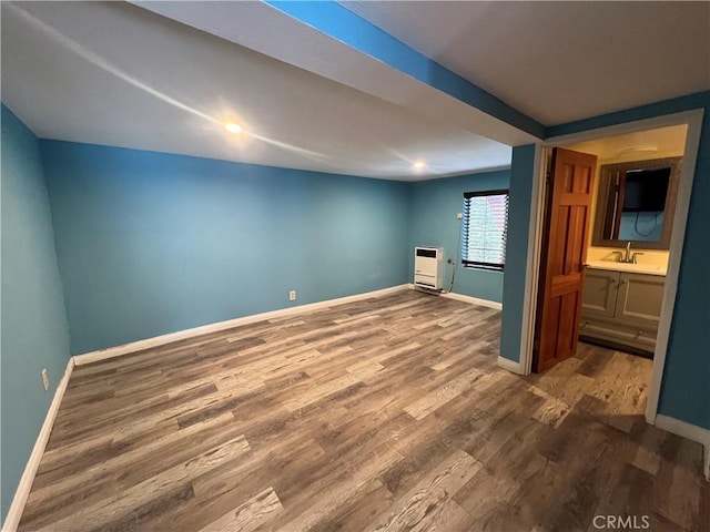 interior space featuring a sink, heating unit, wood finished floors, and baseboards