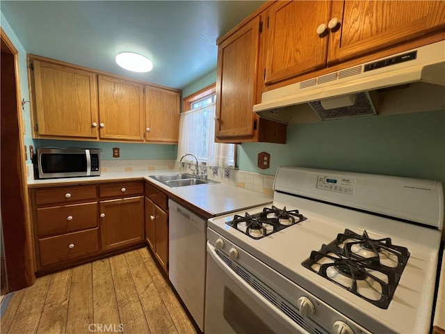 kitchen featuring light wood finished floors, light countertops, a sink, white appliances, and under cabinet range hood