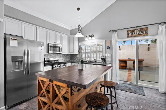 kitchen featuring ornamental molding, stainless steel appliances, vaulted ceiling, dark countertops, and backsplash