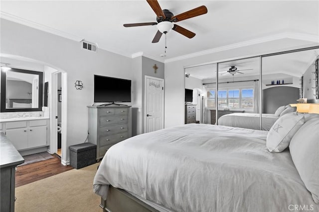 carpeted bedroom with visible vents, connected bathroom, arched walkways, crown molding, and ceiling fan