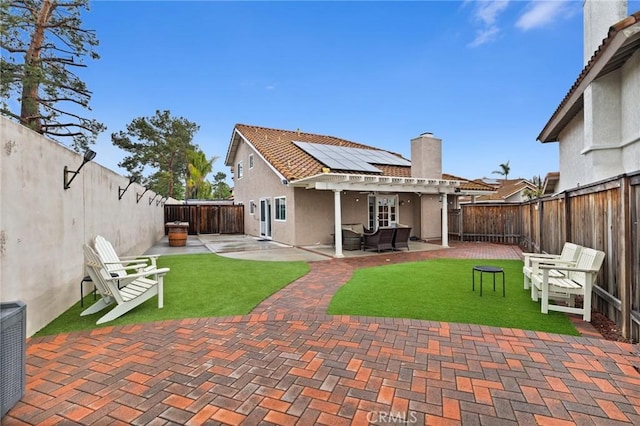 rear view of house with roof mounted solar panels, stucco siding, a fenced backyard, a pergola, and a patio