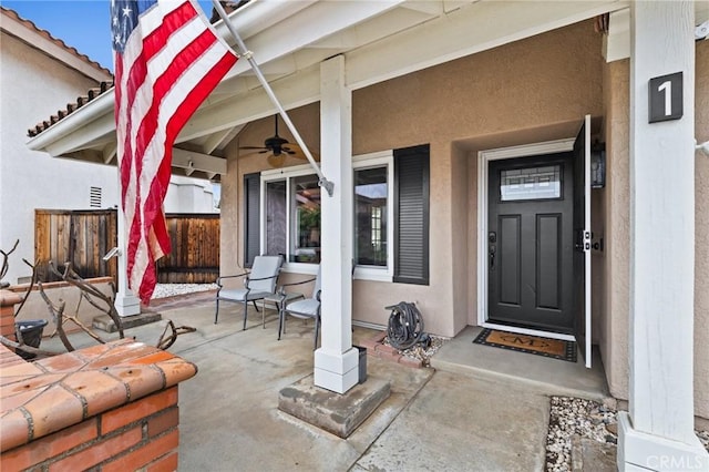 property entrance with ceiling fan, fence, and stucco siding