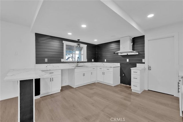 kitchen with light wood-style flooring, island range hood, a sink, white cabinets, and light stone countertops