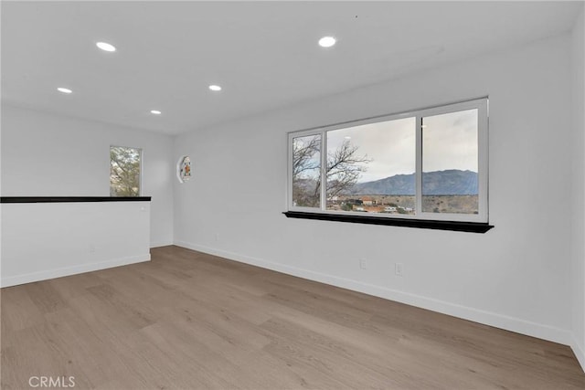 empty room with recessed lighting, a mountain view, baseboards, and wood finished floors