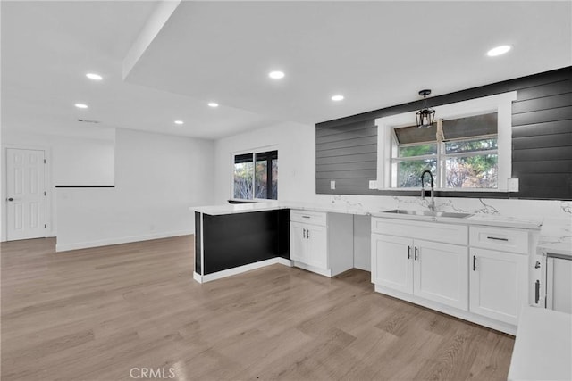 kitchen featuring light stone counters, white cabinets, a sink, light wood-type flooring, and a peninsula