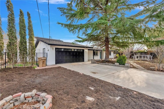 view of front of property featuring stucco siding, concrete driveway, fence, a garage, and a fire pit