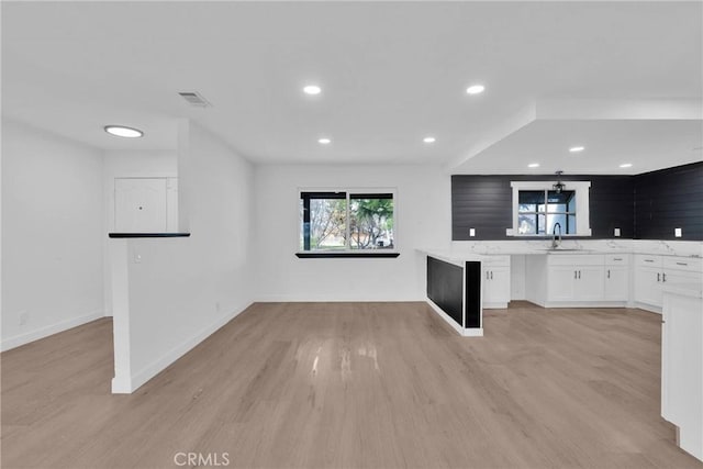 kitchen with baseboards, light wood-type flooring, white cabinetry, a sink, and recessed lighting