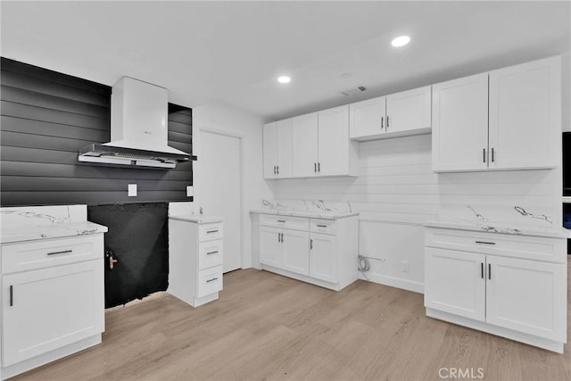 kitchen featuring light stone counters, recessed lighting, white cabinetry, light wood-style floors, and wall chimney range hood