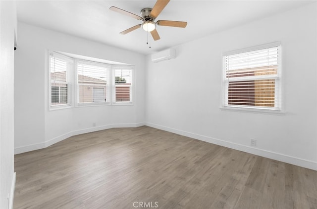 unfurnished room featuring a wall unit AC, ceiling fan, baseboards, and wood finished floors