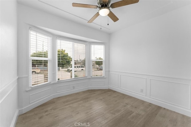 unfurnished room with ceiling fan, light wood-type flooring, and a decorative wall