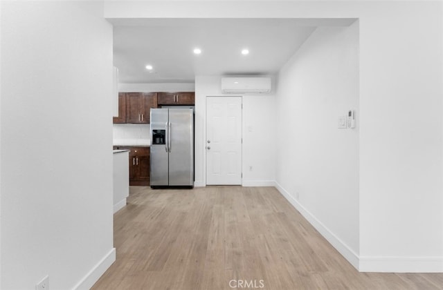 kitchen featuring a wall unit AC, light wood-style floors, baseboards, and stainless steel refrigerator with ice dispenser