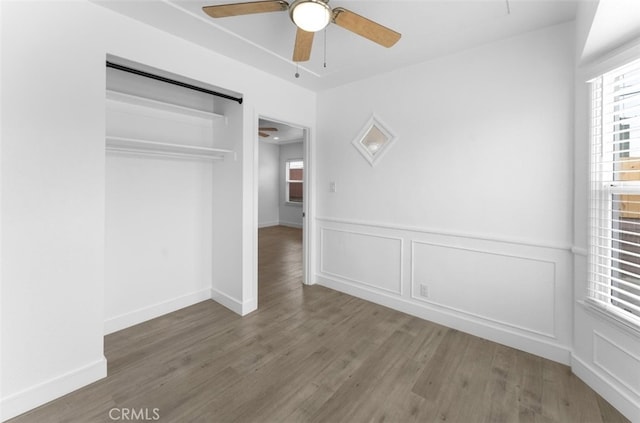 unfurnished bedroom featuring ceiling fan, a wainscoted wall, wood finished floors, a closet, and attic access