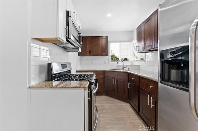 kitchen with light wood-style flooring, appliances with stainless steel finishes, light stone counters, a sink, and backsplash