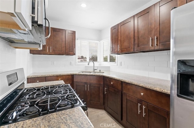 kitchen featuring stainless steel appliances, light stone countertops, a sink, and tasteful backsplash