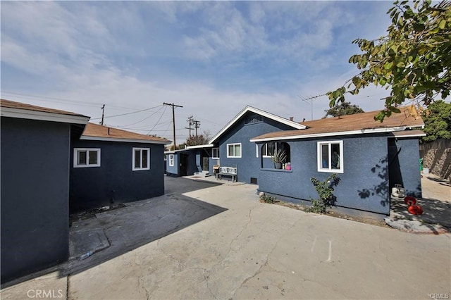 rear view of property featuring driveway, a patio area, fence, and stucco siding