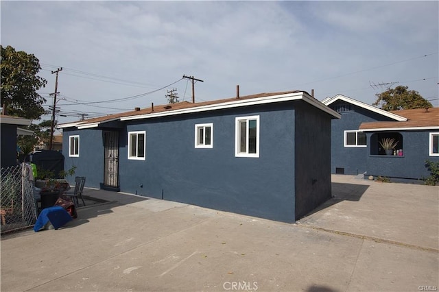 rear view of house with a patio, fence, and stucco siding