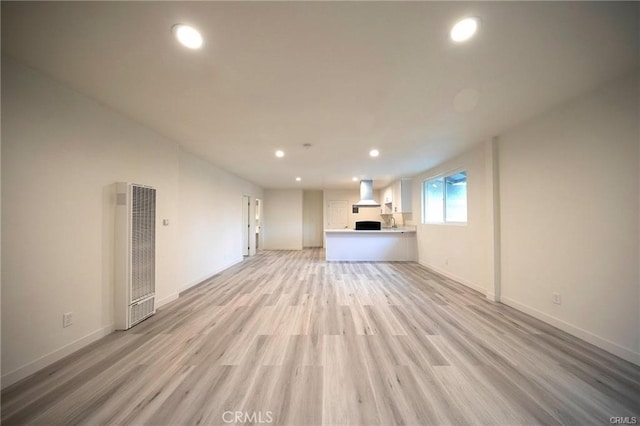 unfurnished living room with light wood finished floors, a heating unit, baseboards, and recessed lighting