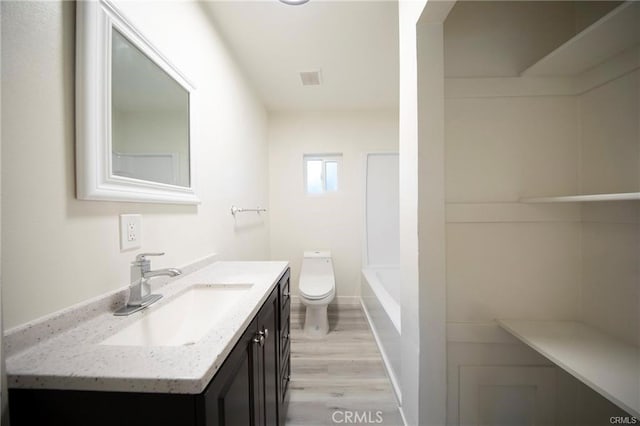 full bathroom with a tub to relax in, visible vents, toilet, vanity, and wood finished floors