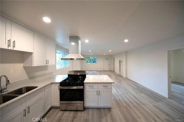 kitchen with a peninsula, a sink, light countertops, island exhaust hood, and gas range