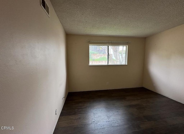 unfurnished room featuring dark wood-style floors, visible vents, and a textured ceiling