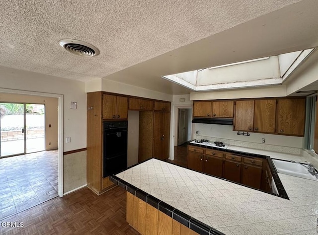 kitchen with a sink, visible vents, a textured ceiling, and brown cabinetry