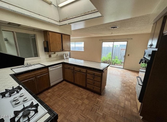 kitchen featuring a sink, a textured ceiling, tile countertops, white appliances, and a peninsula