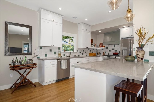 kitchen featuring a breakfast bar, visible vents, appliances with stainless steel finishes, white cabinets, and wall chimney exhaust hood