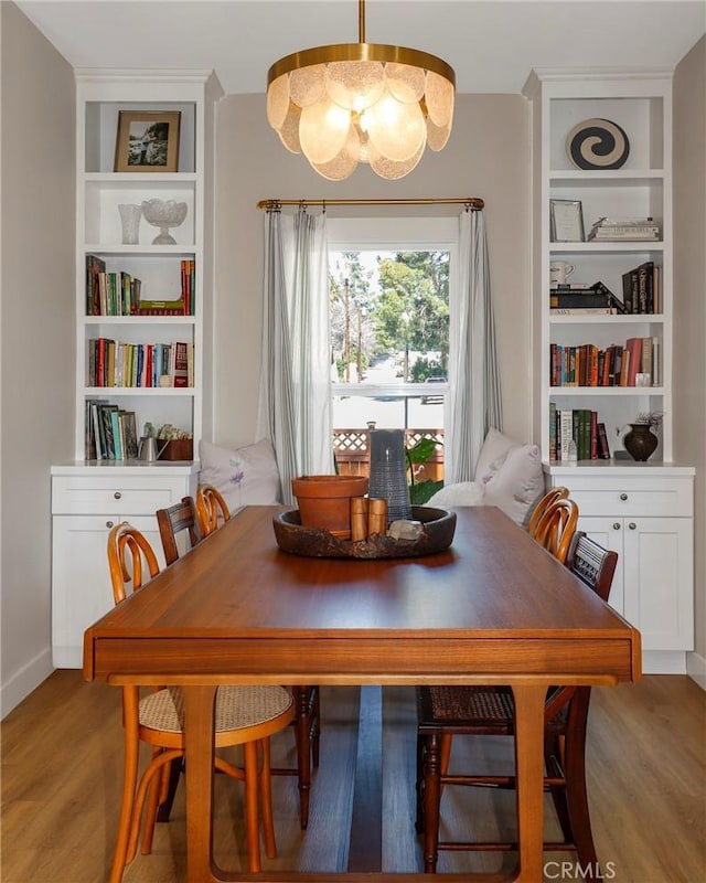 dining room featuring light wood finished floors, built in features, and an inviting chandelier