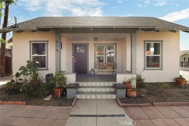 view of front facade featuring a shingled roof, covered porch, and stucco siding