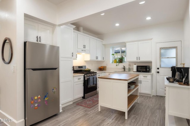 kitchen featuring under cabinet range hood, a sink, white cabinets, appliances with stainless steel finishes, and light wood finished floors