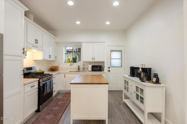 kitchen with white cabinets, butcher block countertops, under cabinet range hood, stainless steel range with gas cooktop, and black microwave