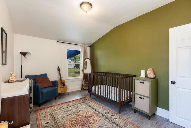 bedroom with a crib, baseboards, vaulted ceiling, and wood finished floors