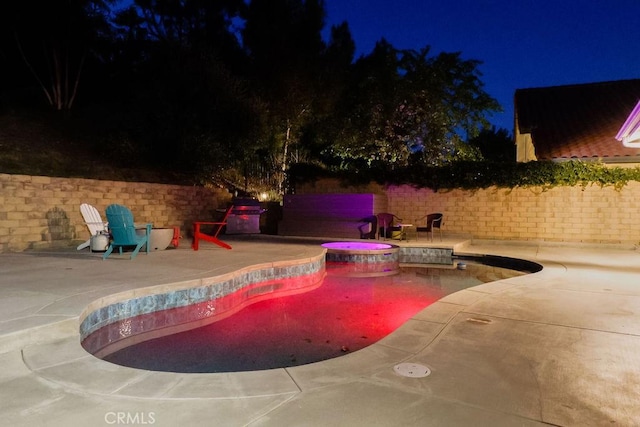 pool at twilight with a pool with connected hot tub, fence, and a patio