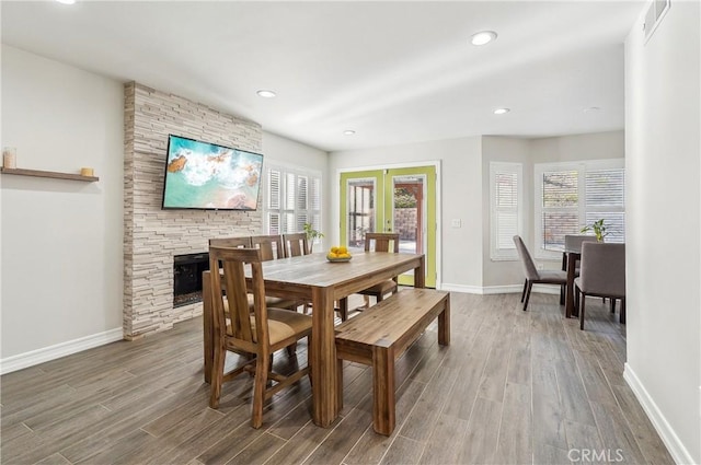 dining area featuring a stone fireplace, french doors, wood finished floors, and baseboards