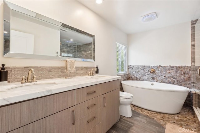 bathroom with a freestanding bath, double vanity, a sink, and tile walls