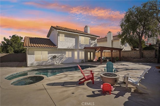 back of property at dusk with stucco siding, an outdoor fire pit, a fenced backyard, and a patio