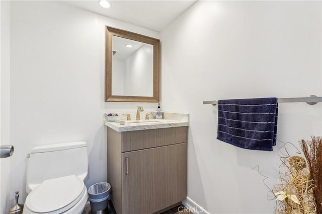 bathroom with toilet, vanity, and recessed lighting