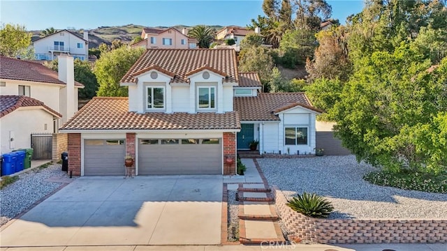 mediterranean / spanish home featuring an attached garage, brick siding, a tile roof, fence, and driveway