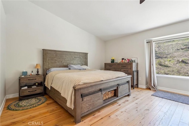 bedroom with vaulted ceiling, light wood-style flooring, and baseboards